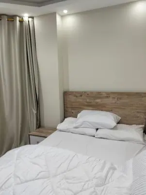 a bedroom with a white bed with a wooden headboard at كومباوند البرنسيسه in Hurghada