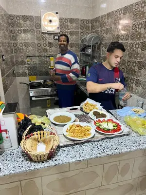 two men standing in a kitchen with food on a counter at Sugar Nubian Guest House Nile Vew in Aswan