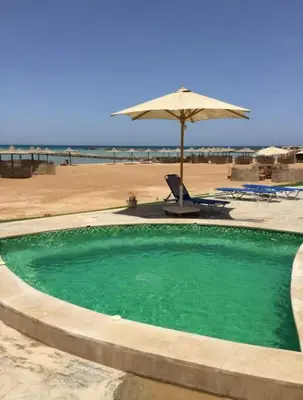 a swimming pool next to a beach with an umbrella at Amaizing 2BR Apartment B2 in Turtles Beach - Hurghada in Hurghada
