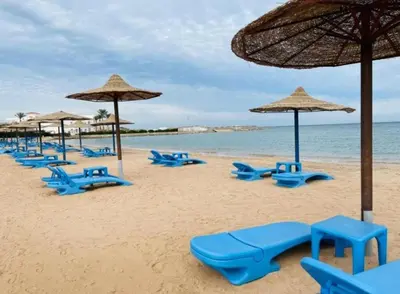 a beach with blue chairs and umbrellas and the ocean at Cecelia Resort in Hurghada