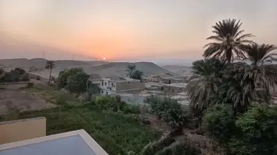 a sunset over a village with palm trees and buildings at Karima house B in Al Aqālitah