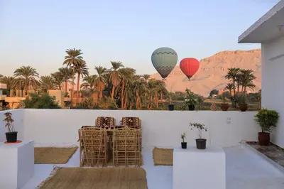 two hot air balloons flying over a desert with palm trees at Akhet House in Luxor
