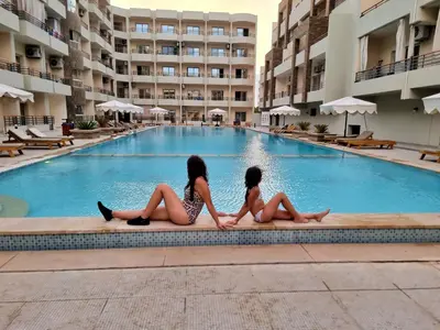 two girls sitting next to a swimming pool at Oasya Studio Hurghada in Hurghada