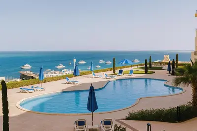 a swimming pool with chairs and umbrellas and the ocean at The View Hurghada Poolfront Sea View Apartment in Hurghada