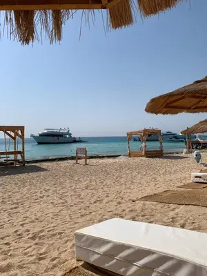 a beach with an umbrella and a boat in the water at Sea Light Arabia on the beach in Hurghada