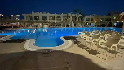 a large swimming pool with white chairs at night at Pause by The Sea Hurghada, Stay, Relax, Repeat in Hurghada