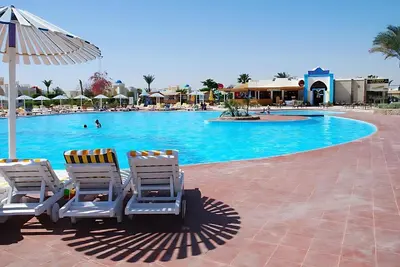 two chairs and an umbrella next to a swimming pool at One Bedroom Chalet Mirage Bay in Hurghada