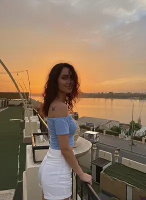 a woman standing on a balcony with the sunset in the background at Jewel Luxor Hotel Nile View in Luxor