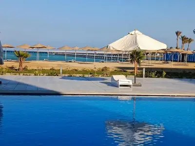 a swimming pool with a white umbrella and a building at Scandic Resort Sea View Room in Hurghada