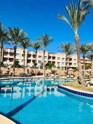 a swimming pool with palm trees and a large building at Stylish & Cozy 50 m2 Studio Chalet in the Sunset Pearl Apartments in Hurghada