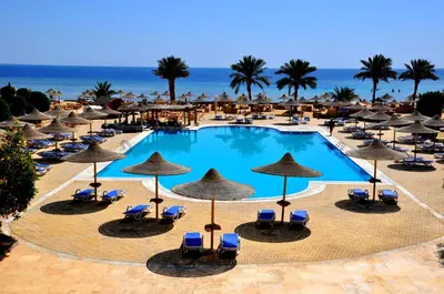 a pool with chairs and umbrellas and the ocean at Shoni Bay Resort in Marsa Alam City