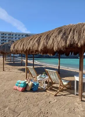 a beach with two chairs and a table and a straw umbrella at Hurghada stylish Apartment on the beach in Hurghada