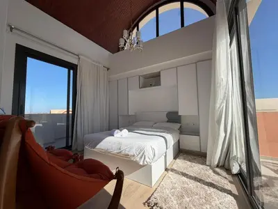 a bedroom with a bed and a chair and a window at Bright Kamaran 2BR | Lofty Ceilings & Pool Access in Hurghada