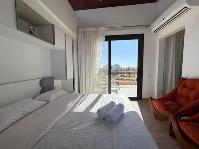 a bedroom with a bed and a chair and a window at Bright Kamaran 2BR | Lofty Ceilings & Pool Access in Hurghada