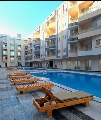 a swimming pool with lounge chairs in front of a building at La bella resort touristic walkway hurghada in Hurghada