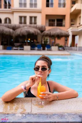 a woman in a bikini holding a drink in front of a pool at Contenintal Rosa Boho Aquapark Hotel 3 Stars in Hurghada