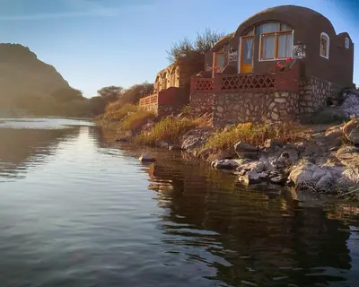 a house sitting on the side of a river at ASSINGAR Island in Aswan