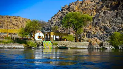 a building on the side of a river with a mountain at ASSINGAR Island in Aswan