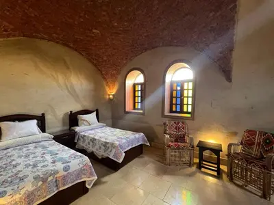a bedroom with two beds and a chair and two windows at Yuhan's Bed & Breakfast in Al Karnak