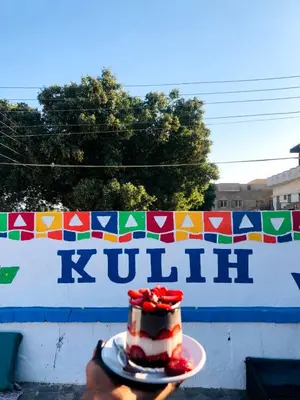 a person holding a piece of cake on a plate at Kuliih guest house in Jazīrat Suhayl