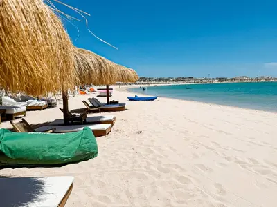 a beach with chairs and straw umbrellas and the water at Amazing 4 BR Villa in Soma Bay Movin Stay in Hurghada
