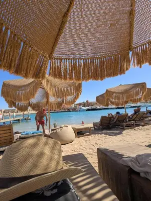 a man standing under an umbrella on a beach at EL GOUNA Boho Beach Chalet with pool access in Hurghada