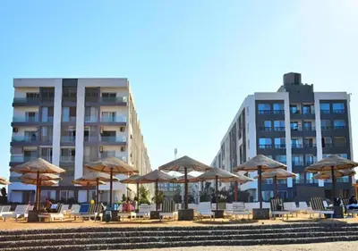 a beach with chairs and umbrellas and a building at Fanadir Bay Beach Resort & Aqua Park in Hurghada