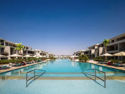 a large swimming pool with chairs and buildings at Rixos Premium Magawish Bay View in Hurghada
