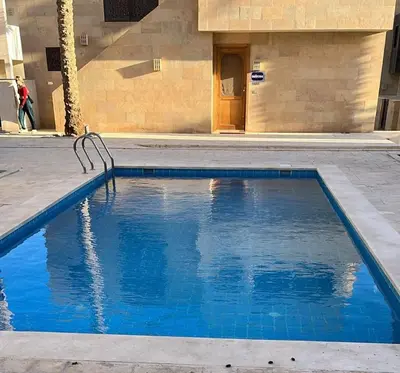 a blue swimming pool in front of a building at Ground Floor 1 Bedroom Scrub Unit in El Gouna in Hurghada