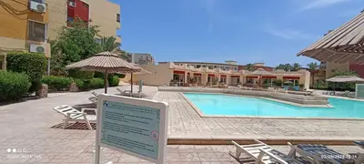 a sign in front of a swimming pool with chairs and umbrellas at 2-Room Apartment with Swimming Pool in Hurghada