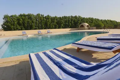 a swimming pool with blue and white striped lounge chairs at Saray El Omda - Egyptian Rural Village in Luxor