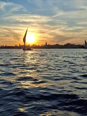 a boat with a sail on the water at sunset at sunrise house in Luxor