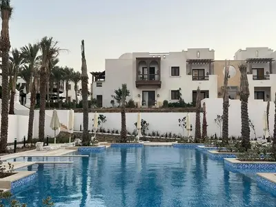 a swimming pool with palm trees in front of a building at Ancient Sands 2BR | Ground Floor, Pool Access in Hurghada