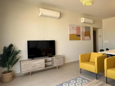 a living room with a television and two yellow chairs at Colorful 1BR Apt-Free Pool & Lagoon Access In ElGouna in Hurghada