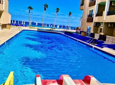 a large swimming pool next to a building with palm trees at Sea view studio for rent at Juliana at Hurghada in Hurghada