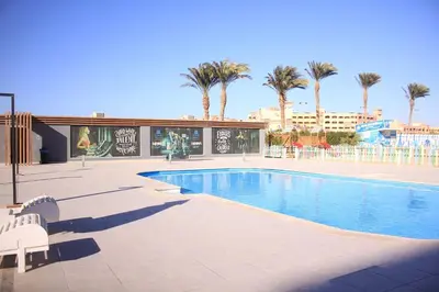 a swimming pool with two white chairs and palm trees at Scandic resort near diving center Colona Divers Hotel Room in Hurghada