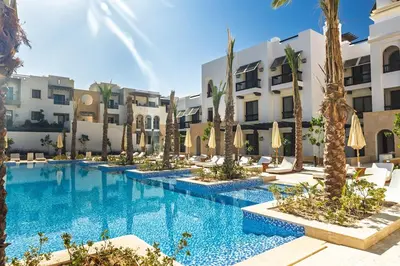 a hotel pool with palm trees and umbrellas at Stylishly furnished and quietly located apartment in Hurghada