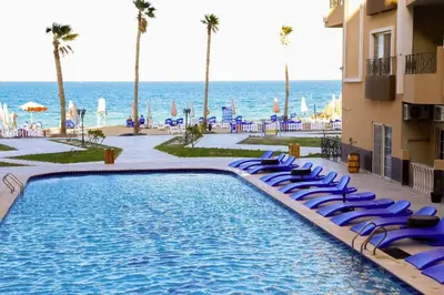 a swimming pool with blue lounge chairs and the ocean at Juliana Beach Resort, Hurghada in Hurghada