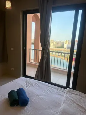 a bed with two blue pillows on it in front of a window at Yoke 2 bedrooms Duplex Tawila ElGouna, Plaza gouna in Hurghada