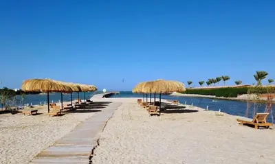 a beach with chairs and straw umbrellas and the water at Balkan Beach Resort- Relaxing Beach Apartment in Hurghada