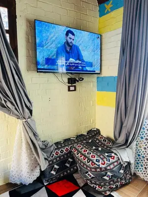 a tv hanging on a wall with a bed with glasses at Marwa House an Authentic Mud-Brick Home in Al Aqālitah