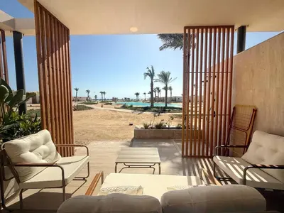 a living room with chairs and a patio with a beach at Pool front Mesca Cabana Minutes to Sandy Beach in Soma bay in Hurghada