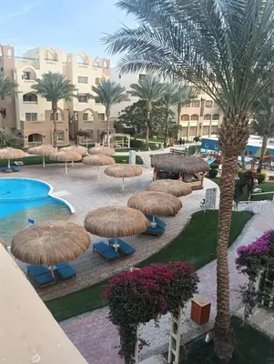 a resort with a pool and umbrellas and palm trees at Karma Apartment in Hurghada