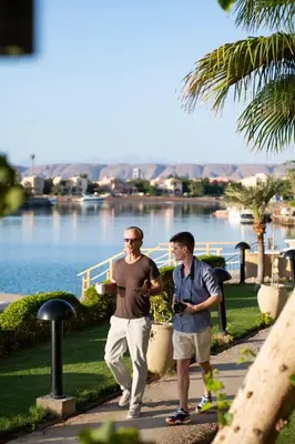two men walking down a sidewalk near a body of water at Three Corners Ocean View El Gouna - Adults Only in Hurghada
