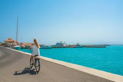 a woman riding a bike down a road next to the water at Kempinski Hotel Soma Bay in Hurghada