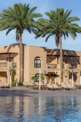 two palm trees in front of a building with a pool at JAZ Lamaya Resort in Coraya Bay