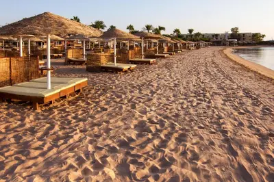 a beach with a row of umbrellas and benches at Eagles Paradise Abu Soma Resort in Hurghada