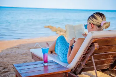a woman sitting in a chair reading a book on the beach at Caves Beach Resort Adults Only in Hurghada