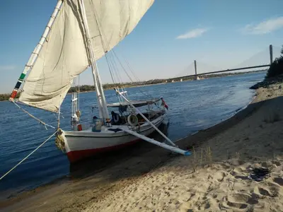 a boat sitting on the beach with a bridge in the background at The Mango Guest House in Aswan