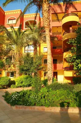 a yellow building with palm trees in front of it at Esplanada Beach Apartment, no single men in Hurghada